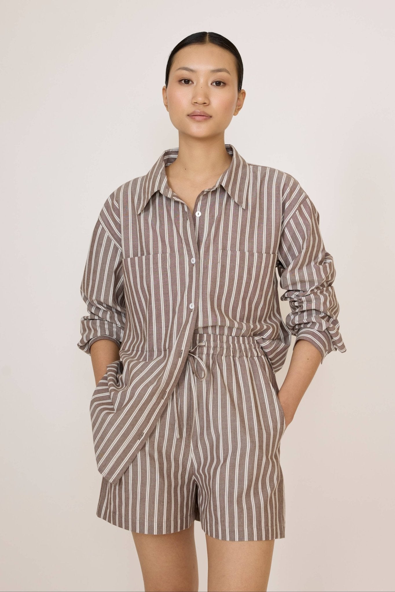 Woman wearing a Laude Everything Shirt in Acorn Stripe and matching shorts set on a plain background