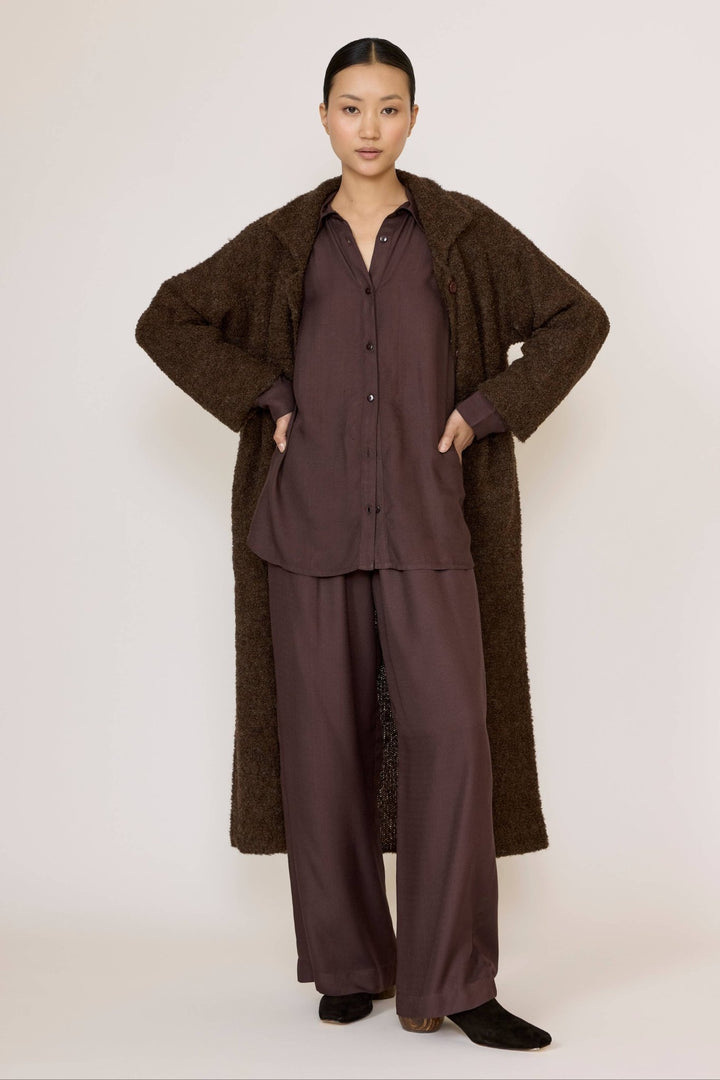 Woman wearing a Laude Everything Shirt in Chocolate Brown with brown pants and a long brown coat with a neutral background