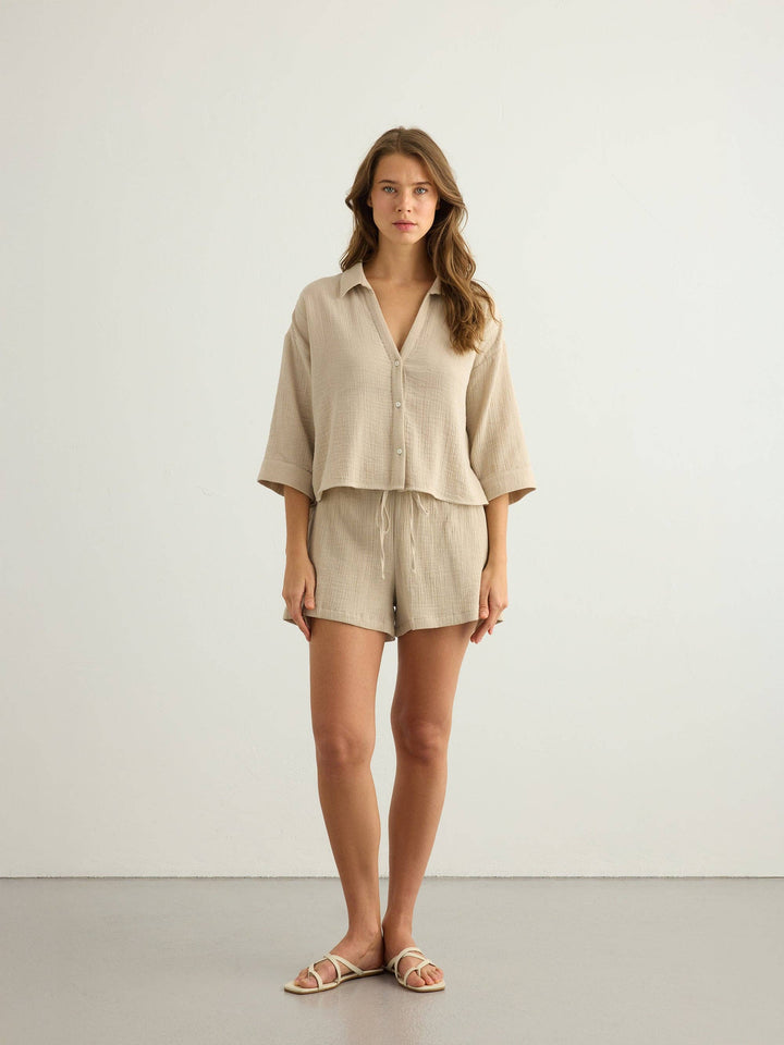 Woman wearing a Handloom Aura oatmeal button-up shirt and shorts on a plain background