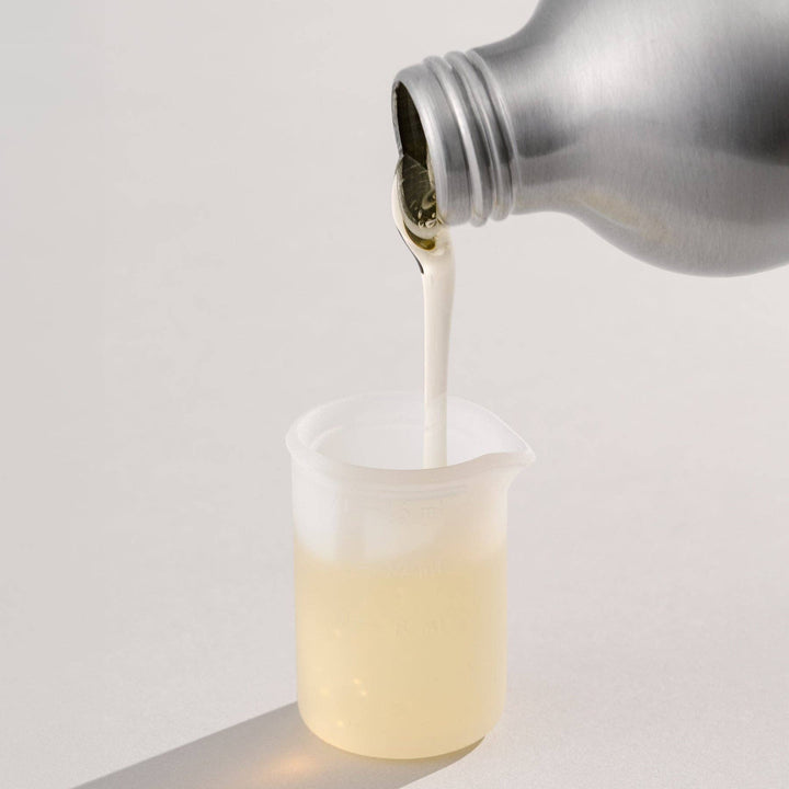Bottle of detergent pouring into a measuring cup on a light gray background