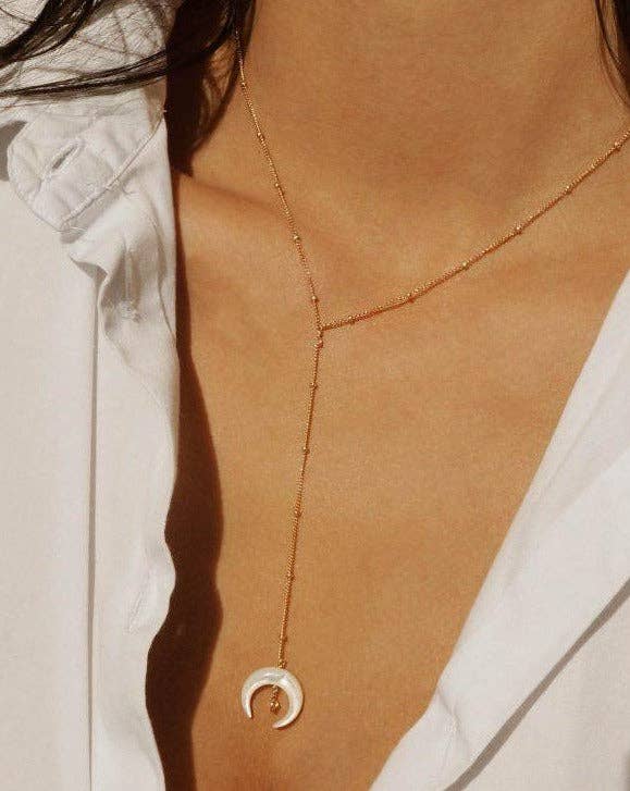 Necklace with a crescent moon pendant on a person wearing a white shirt.