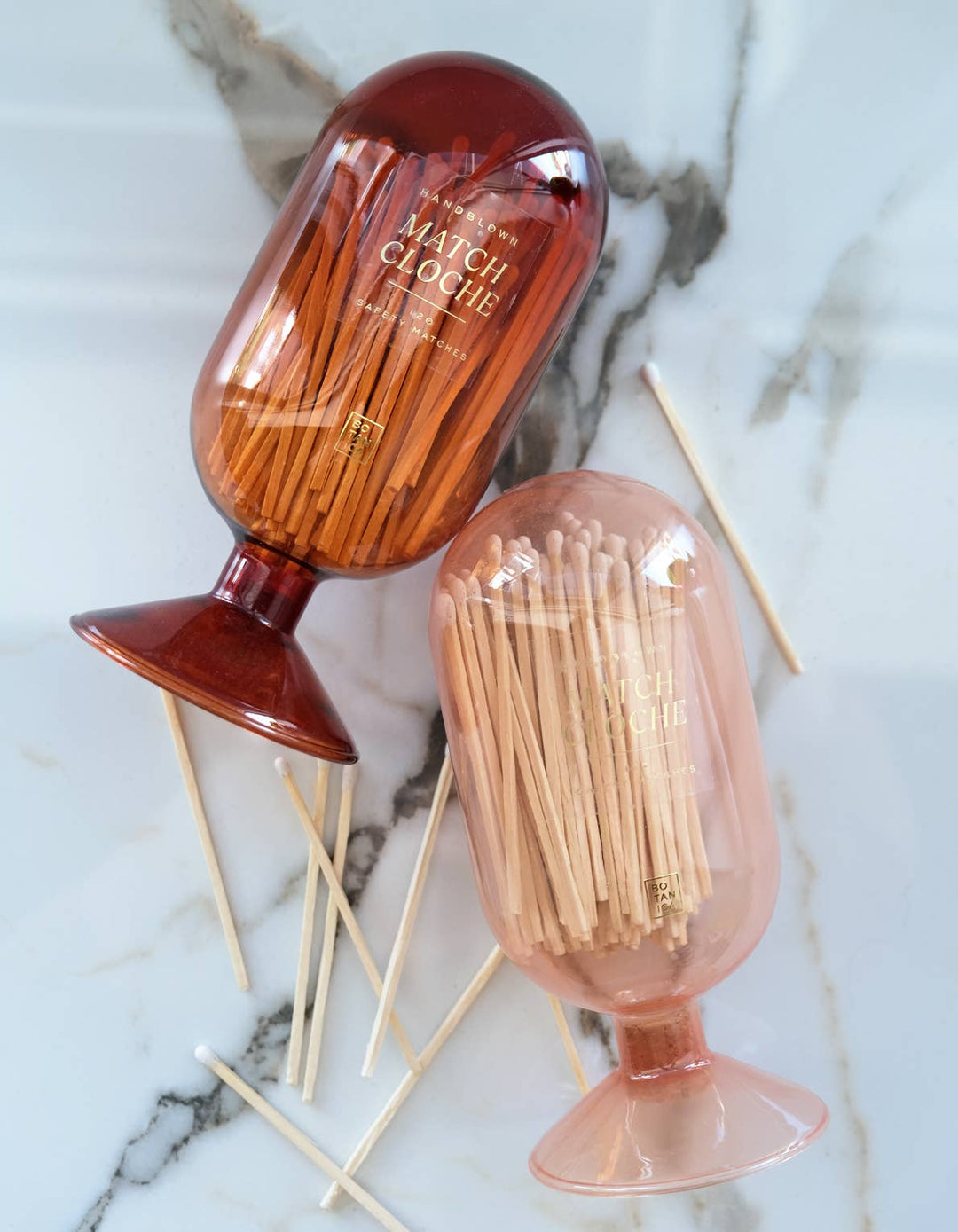 Two vintage-style match cloches with matches on a marble surface