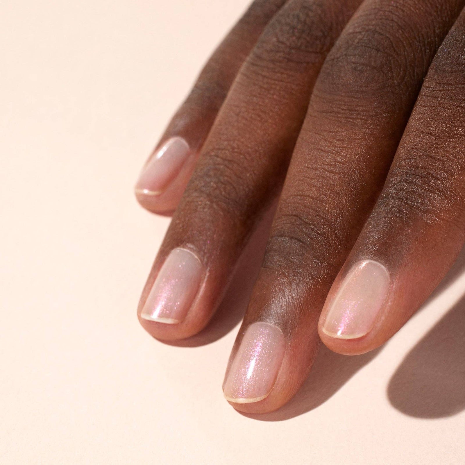 Close-up of a hand with glazed effect powder on nails on a beige background