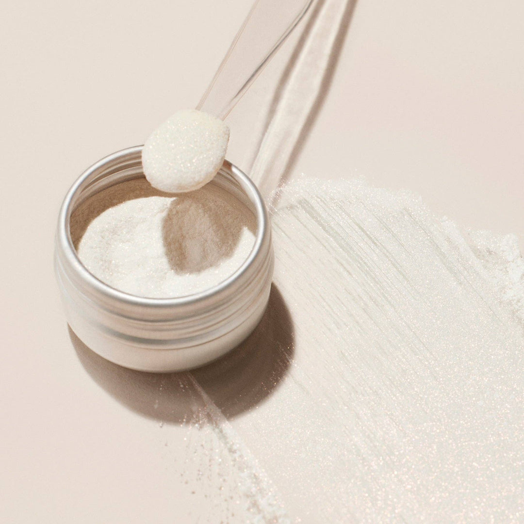 Jar of white glazed effect powder with a spoon on a beige background