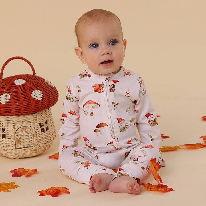 Baby wearing a Gnomes Organic Snugglesuit Convertible Romper sitting next to a wicker basket and fall leaves on a beige background.