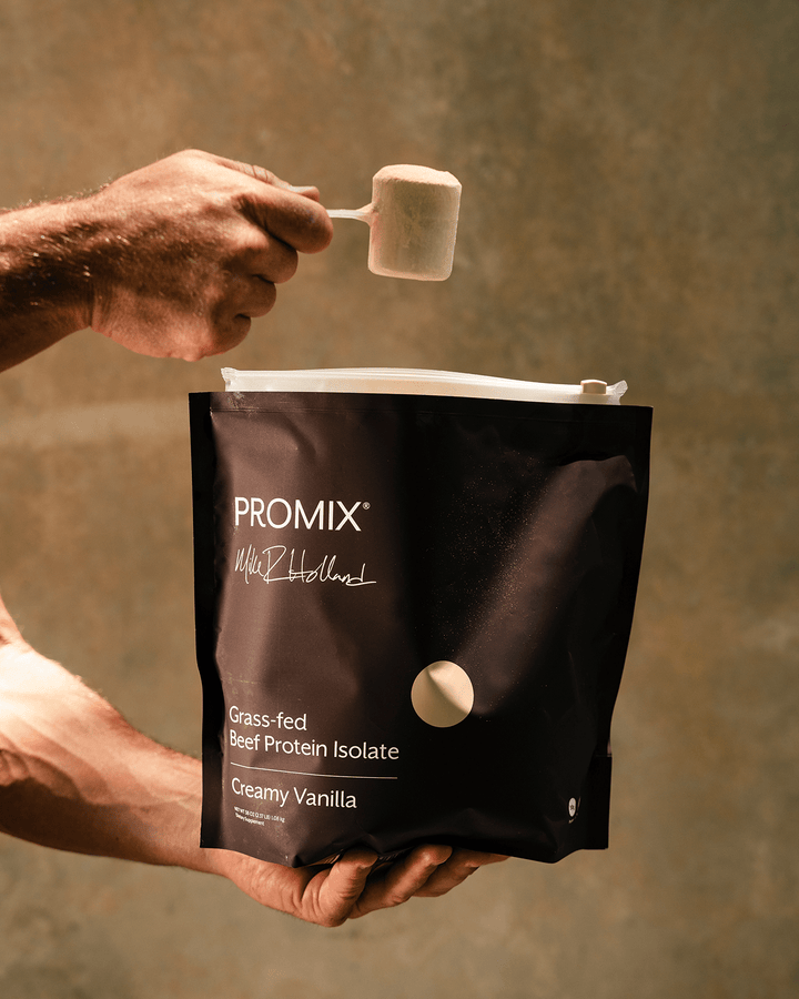 A person holds a brown PROMIX protein powder bag while pouring a scoop of creamy vanilla protein powder from a scoop above the bag, against a warm, textured brown background.