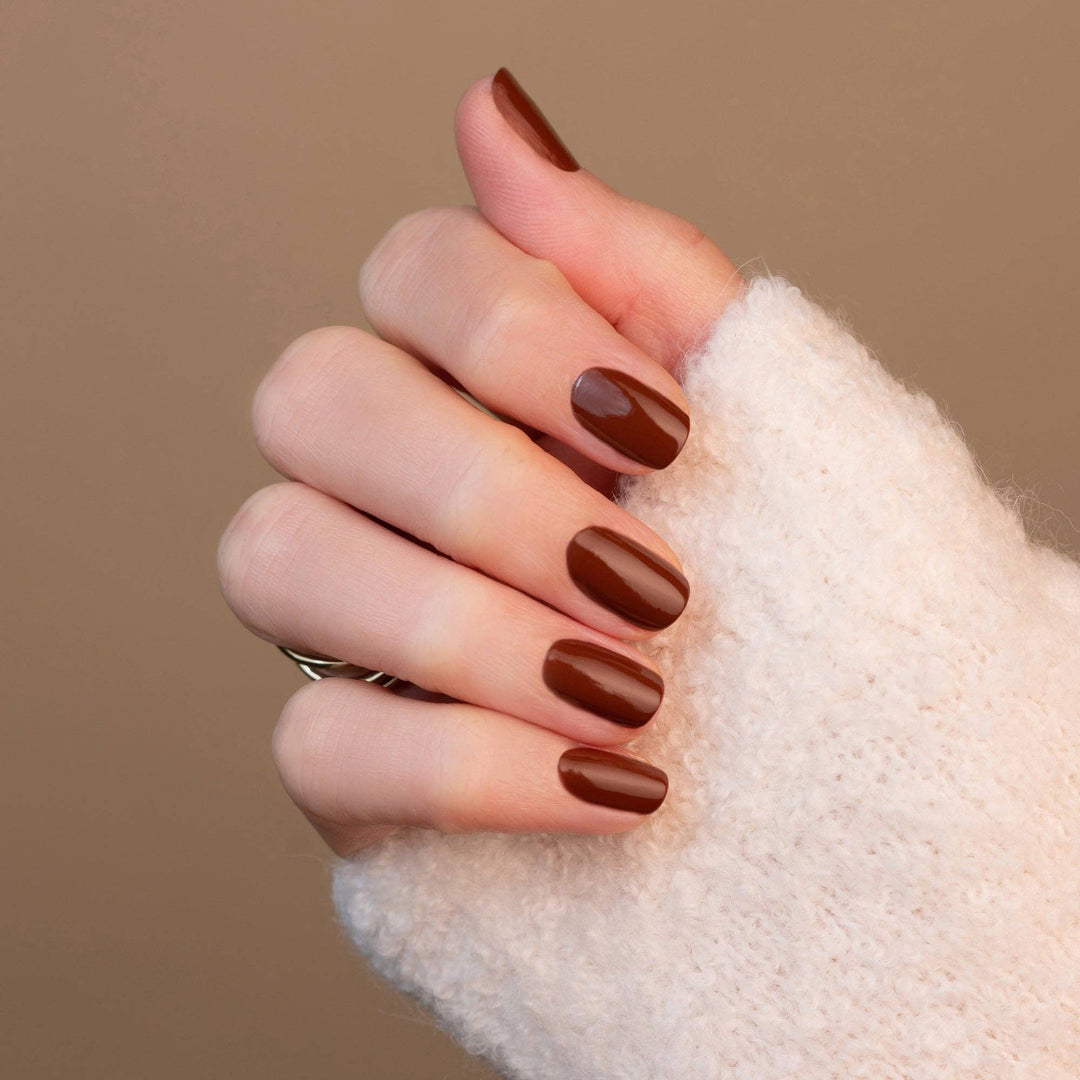 Hand with brown nail polish on a beige background