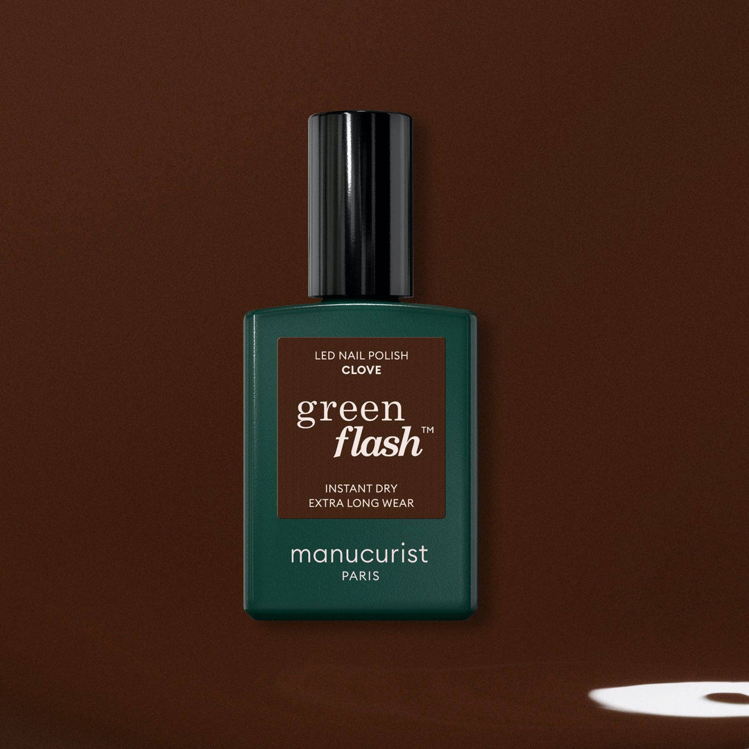 A bottle of manucurist Green Flash LED nail polish glove in a dark green color, set against a solid dark brown background.