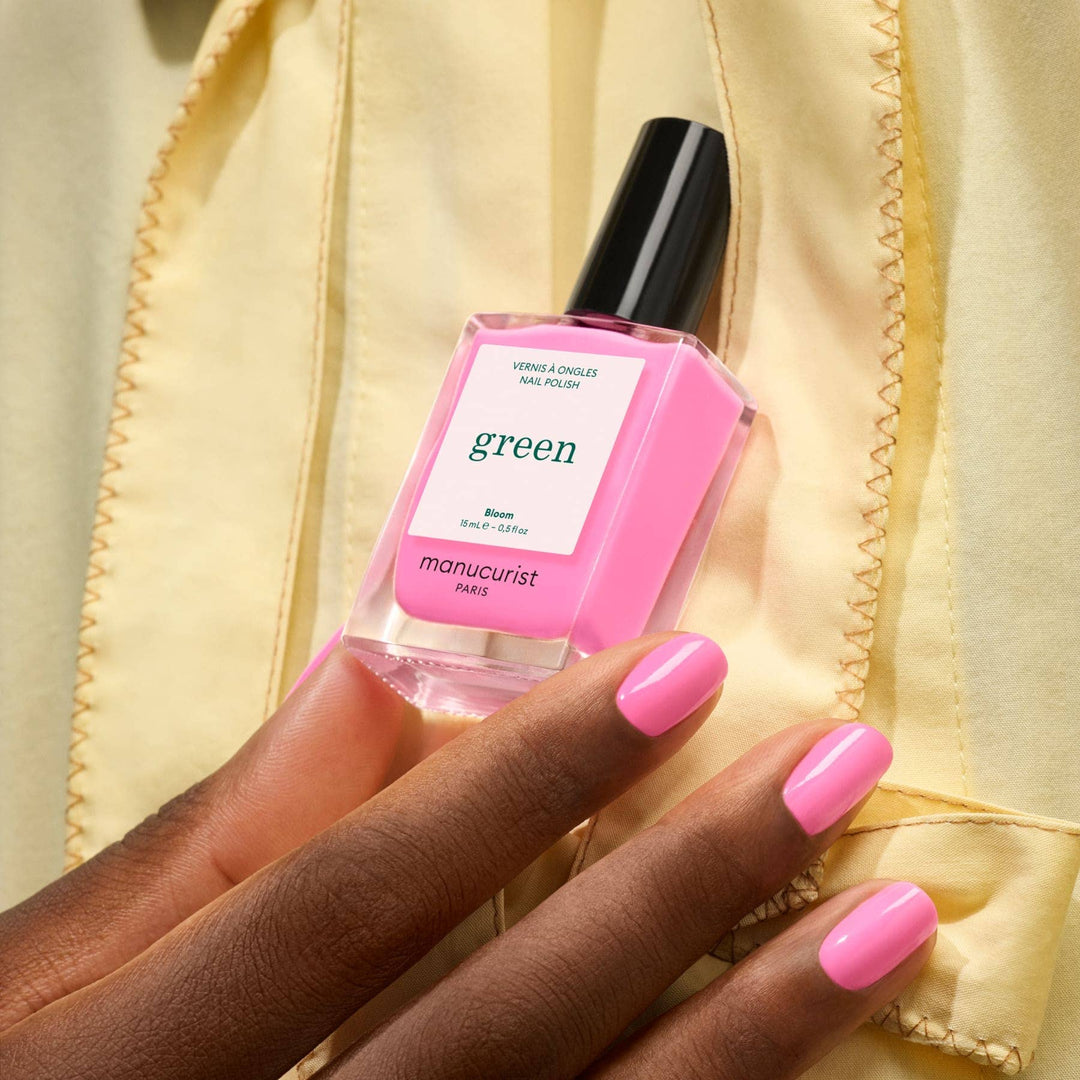 Hand holding a pink nail polish bottle labeled &