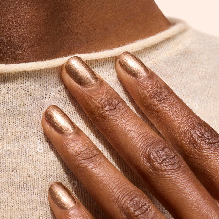 Close-up of a hand with bronze nail polish on a beige fabric background