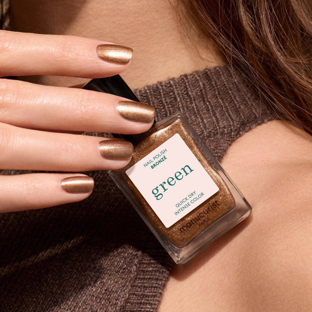 Nail polish with bronze nail polish bottle held by a hand wearing the polish