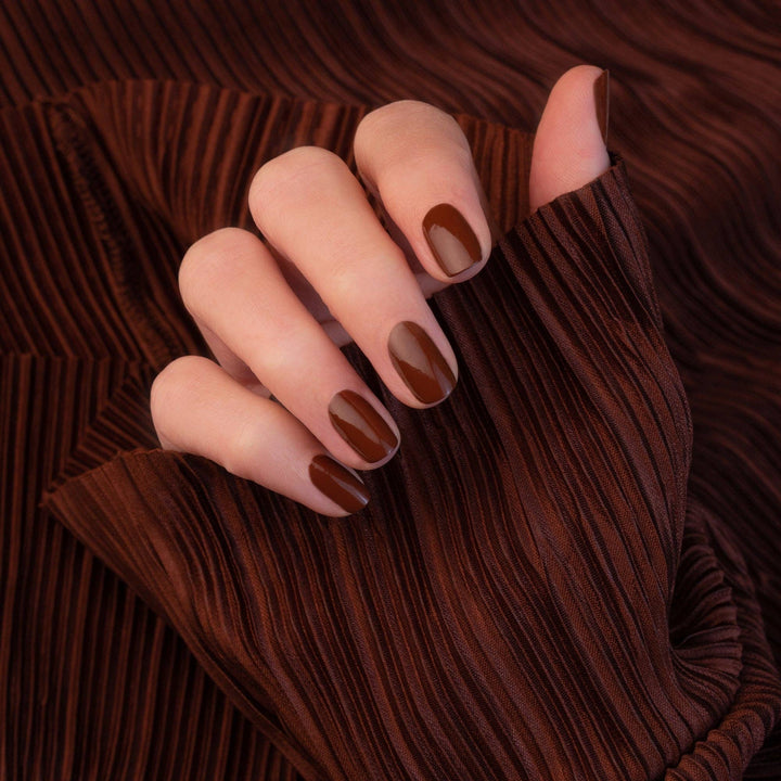 Hand with chestnut nail polish on a brown textured background