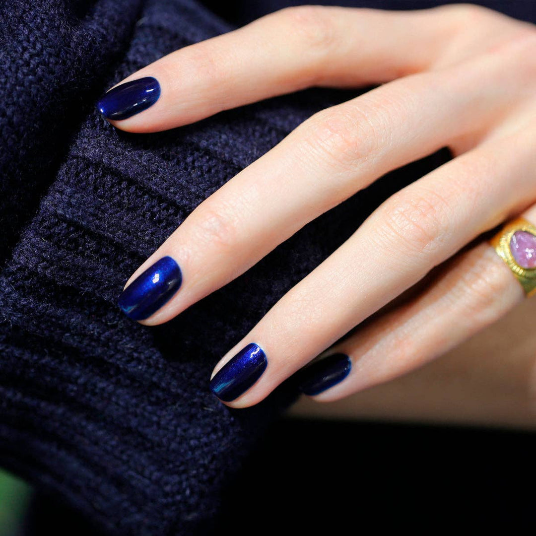 Close-up of a hand with dark blue nail polish on a dark textured background