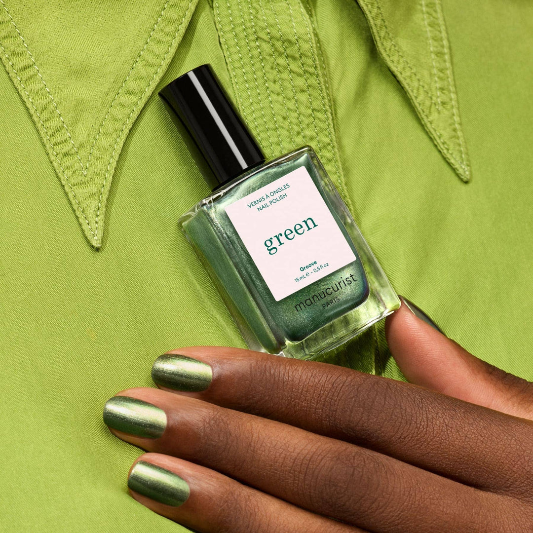 Green nail polish bottle with a hand showcasing green nails against a green background