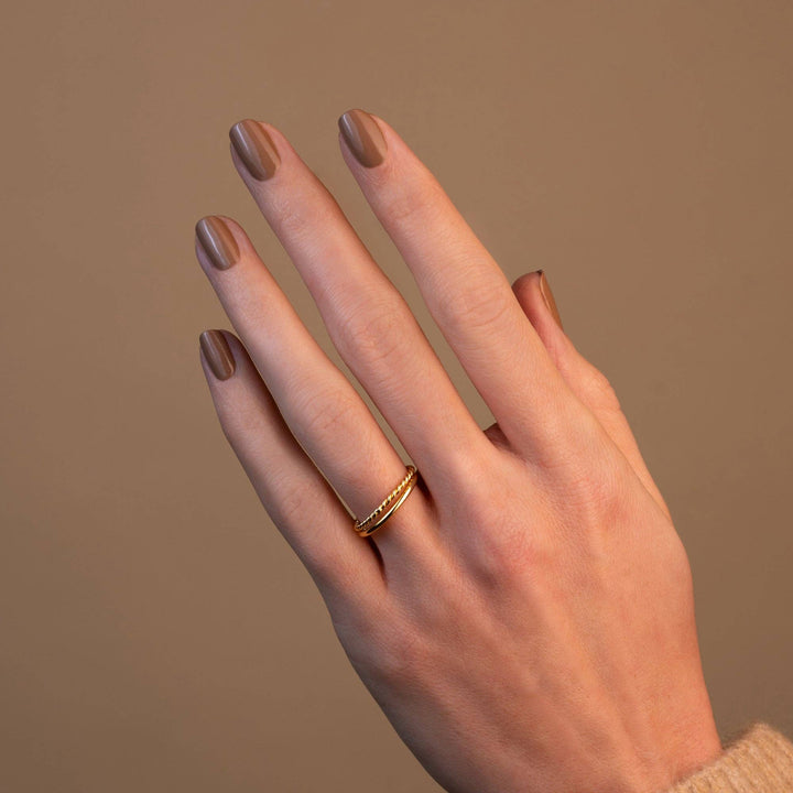 Hand with a gold ring wearing elm nail polish on a beige background