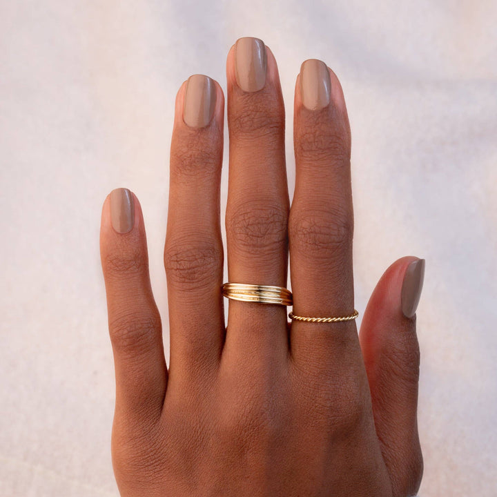 Hand with gold rings wearing elm nail polish on a neutral background