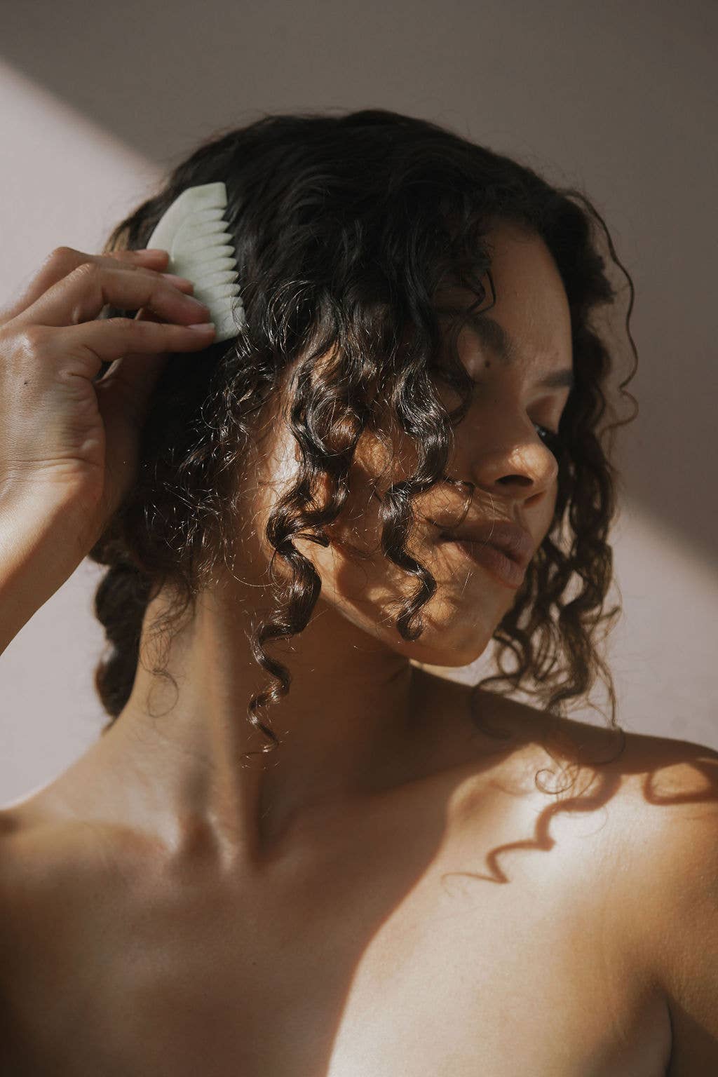 Person combing their curly hair with a Jade comb against a neutral background