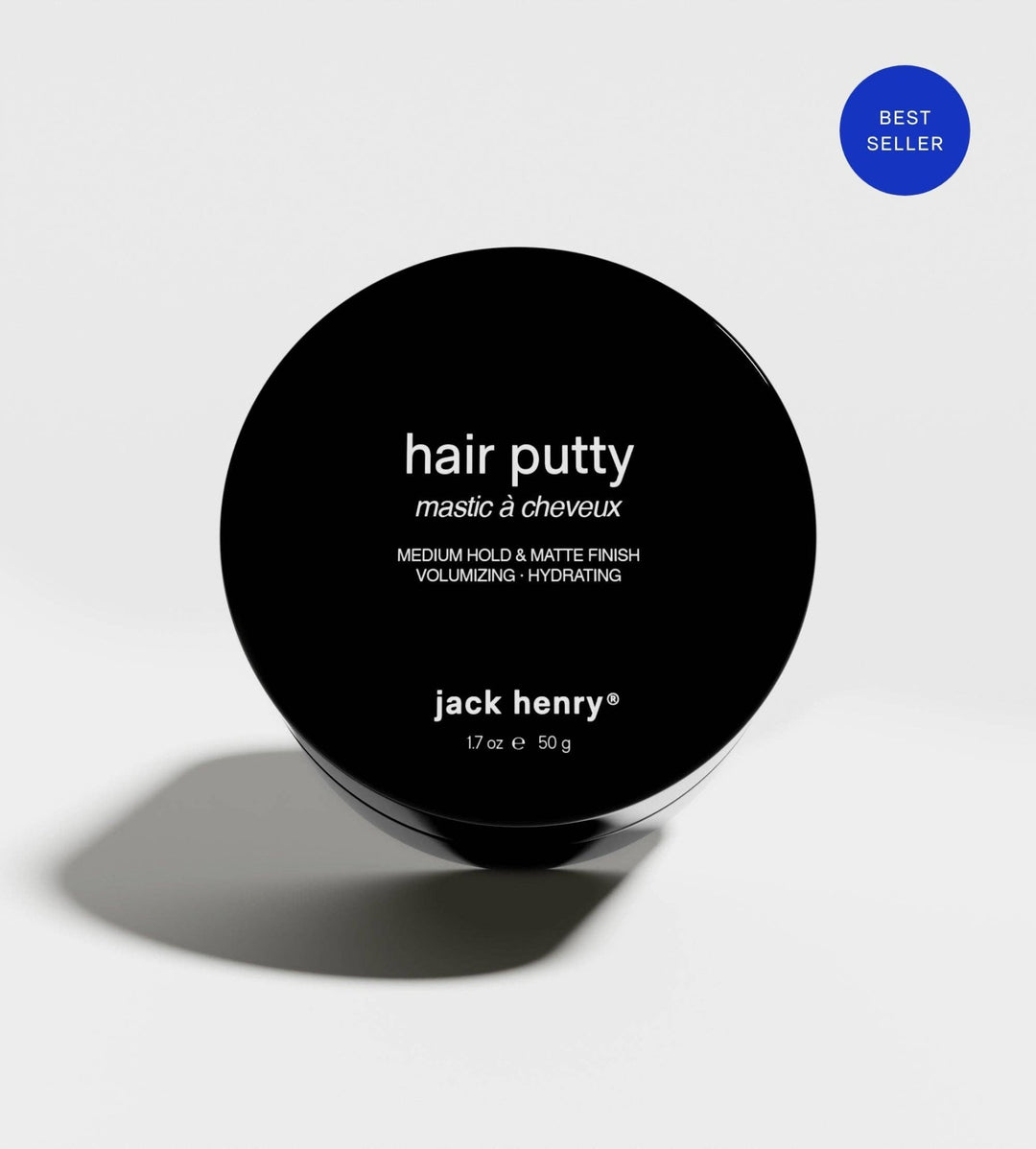 A round black jar lid for Jack Henry Hair Putty, featuring white text, set against a light gray background with a soft shadow and a blue &