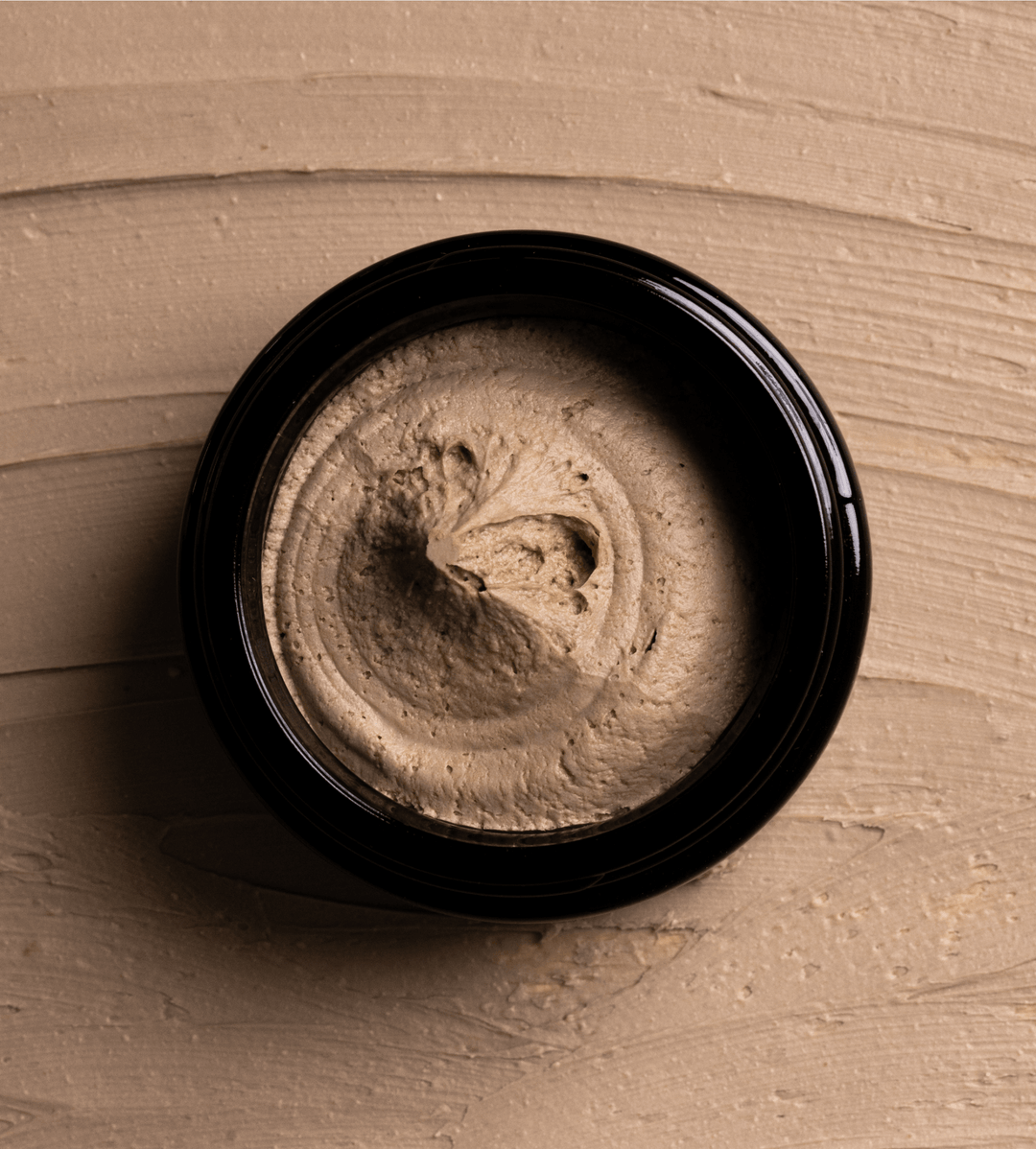Open jar of jack henry hair putty on a beige textured background.