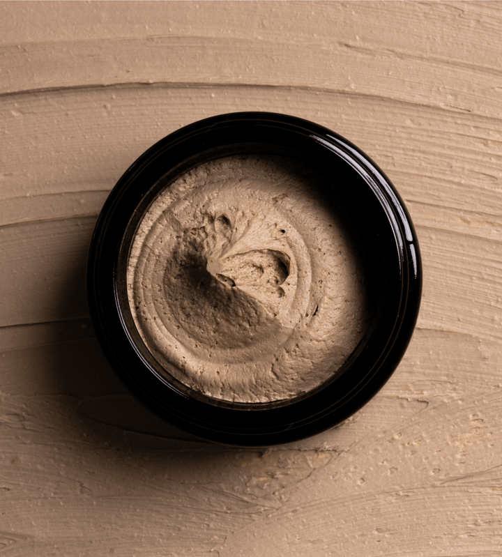 Open jar of jack henry hair putty on a beige textured background.