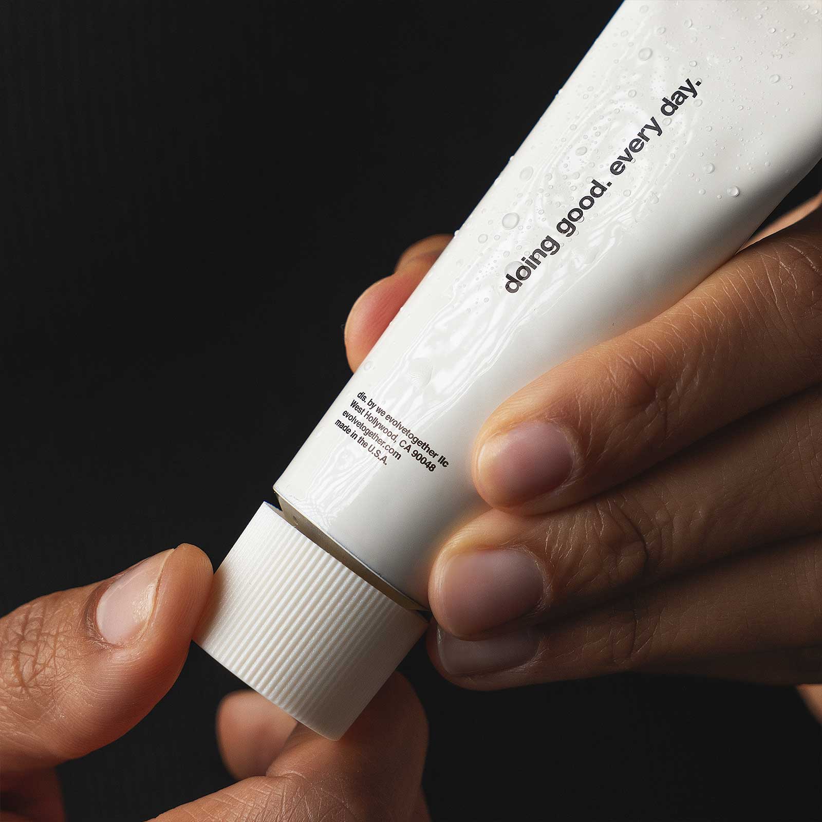 Hand holding a white tube of hand cream with text on a black background