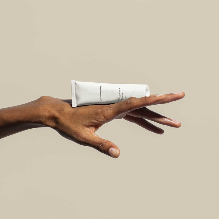 Hand holding a white tube of cream against a beige background