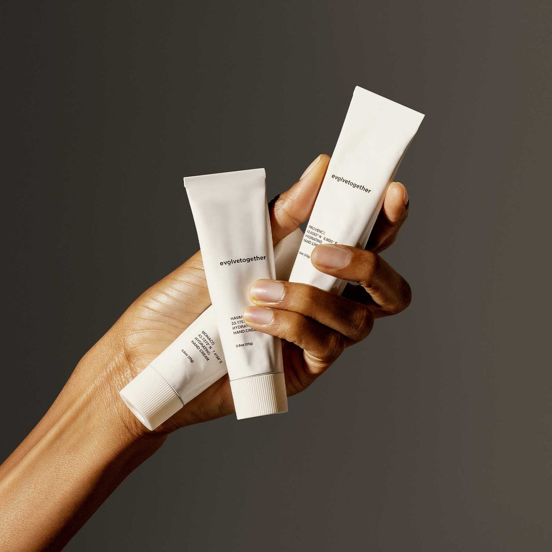 Hand holding three tubes of hand cream against a dark background