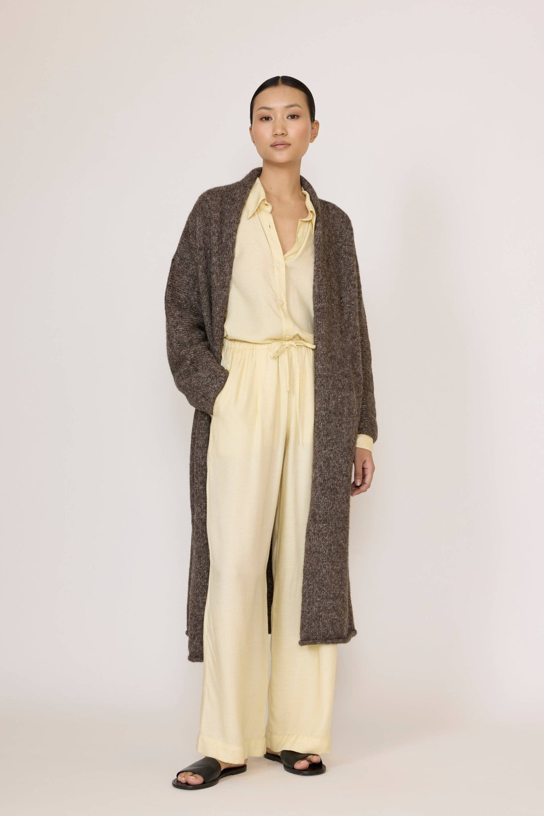 Person wearing a Laude Heirloom Sweater Coat in Nutty Brown over a light yellow shirt and pants on a white background