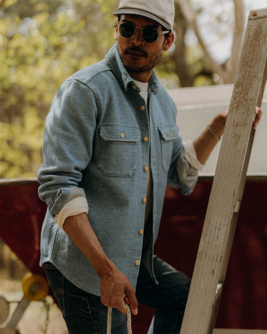 Man in a denim shirt and cap holding a wooden board outdoors