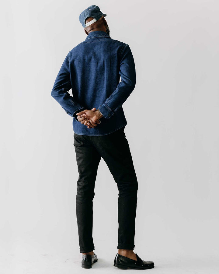 Person wearing a blue jacket and black pants standing against a plain background