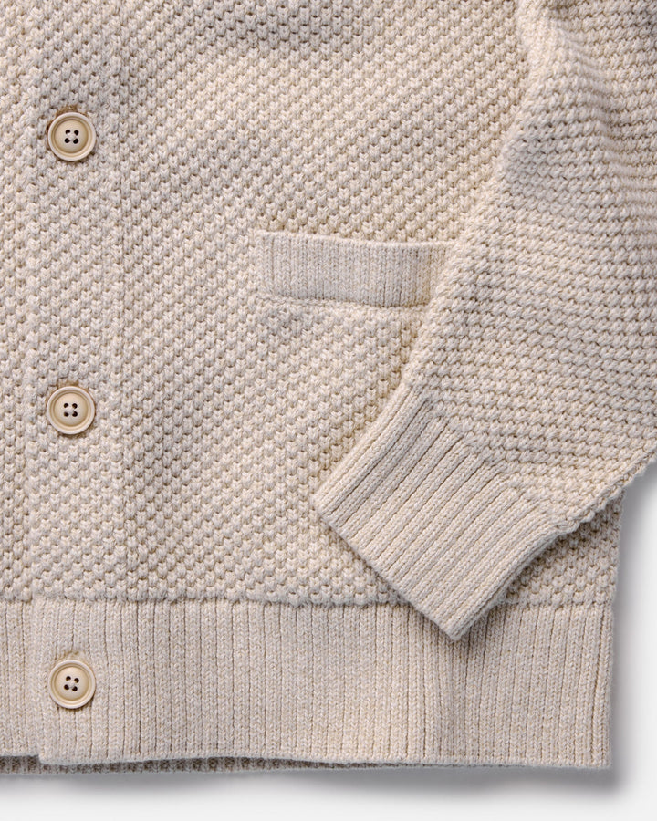 Close-up of a beige knitted cardigan with button details on a white background