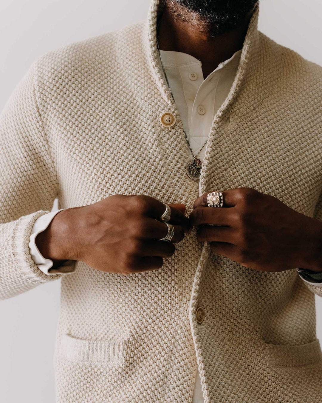 Person wearing a beige knitted cardigan with a plain background