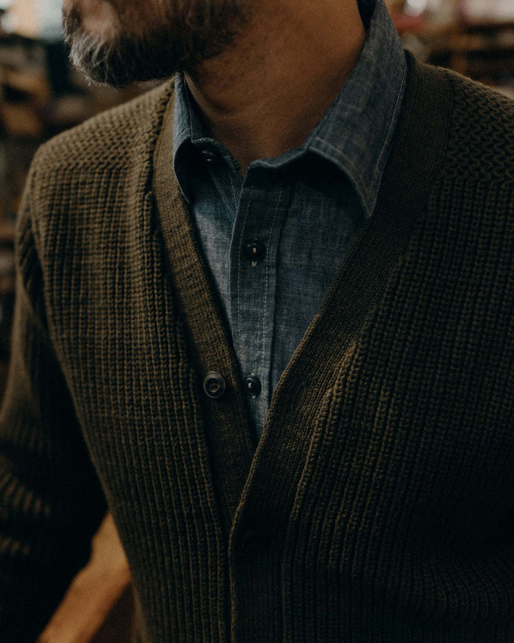 Man wearing a green sweater over a blue shirt with a blurred background