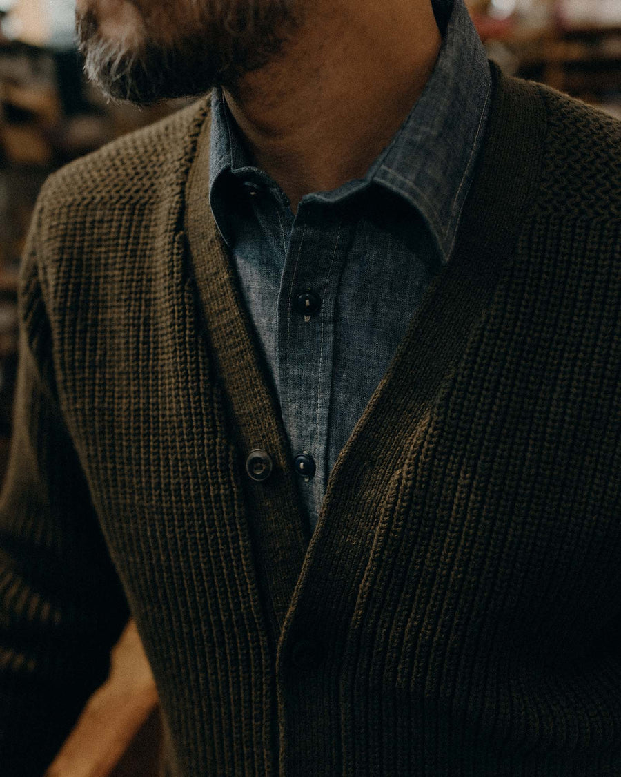 Man wearing a green sweater over a blue shirt with a blurred background