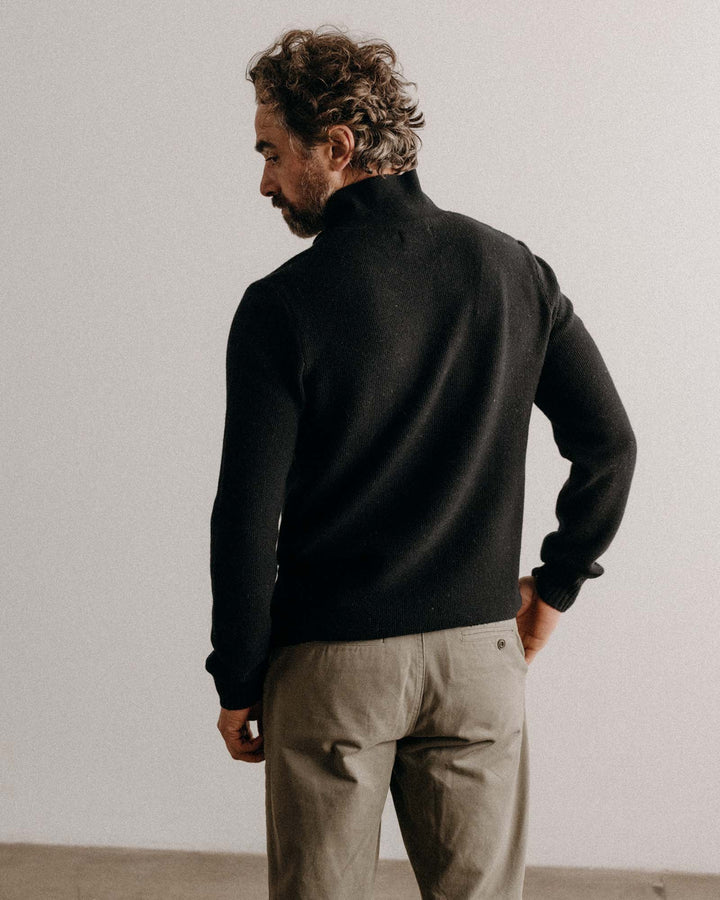 Man wearing a midnight sweater and beige pants against a plain background