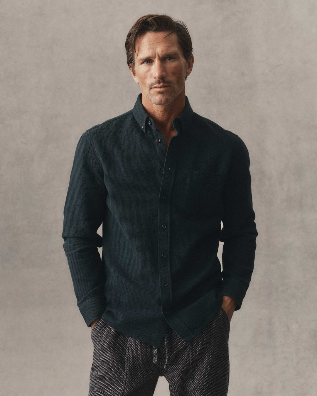 A man wearing The Jack in Forest Waffle and textured gray pants, standing against a neutral textured gray background.