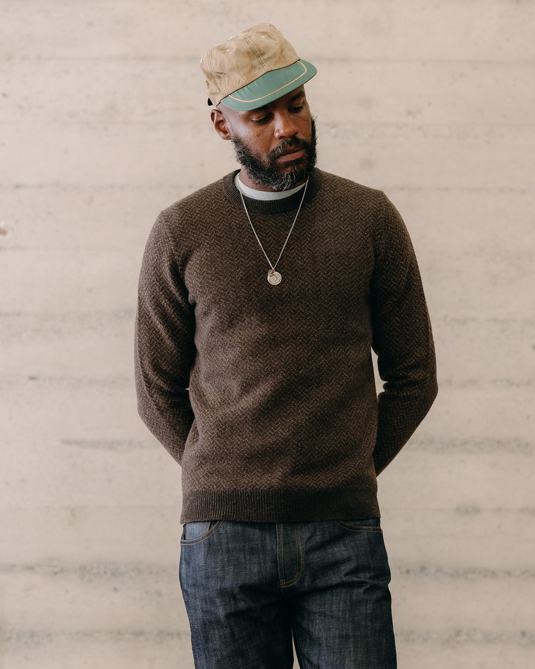Man wearing a brown sweater and cap against a light gray wall