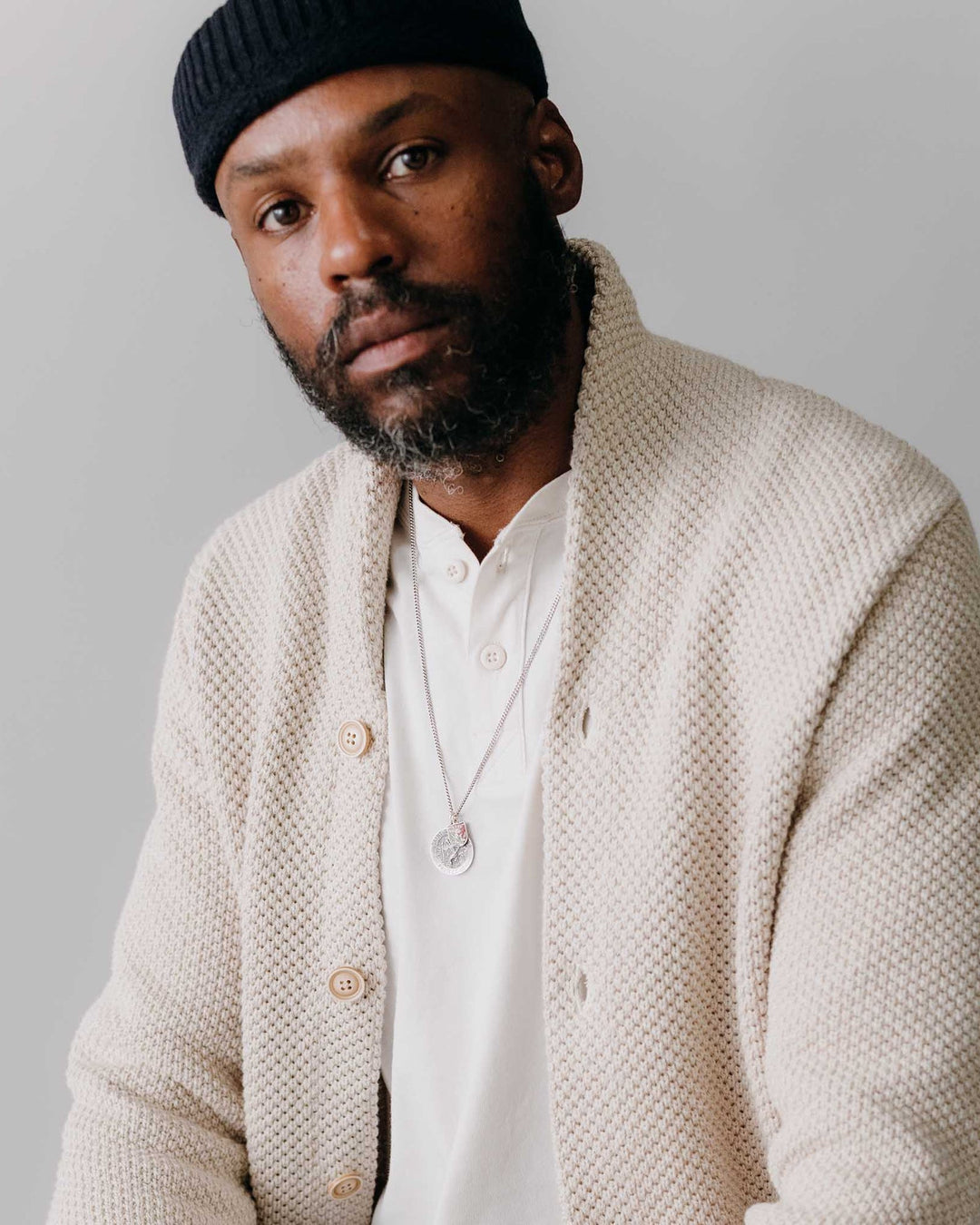 Man wearing a beige cardigan over a white shirt with a plain background