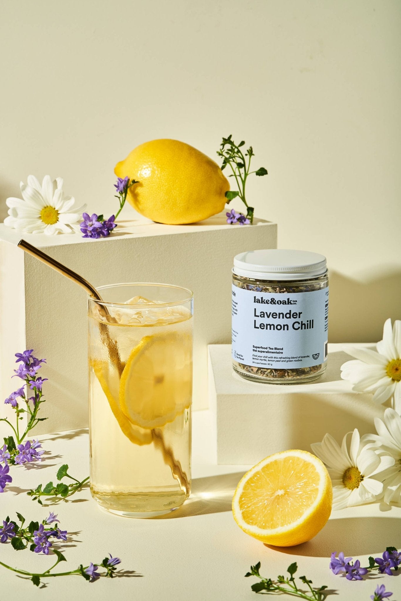 Glass of iced tea with lemon slices, jar of 'Lavender Lemon Chill' tea, and lemons on a light background.