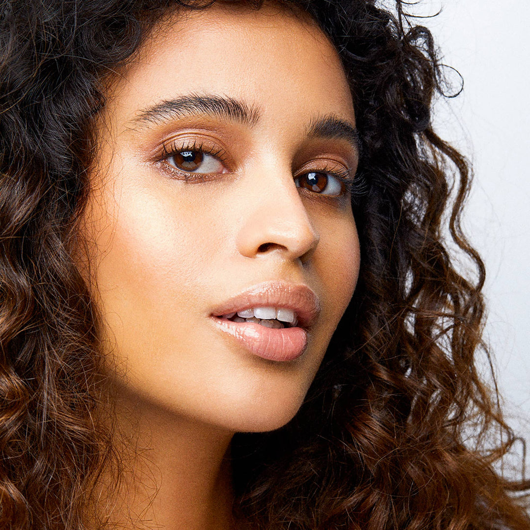 Close-up of a woman with curly hair and hydrated lips against a neutral background