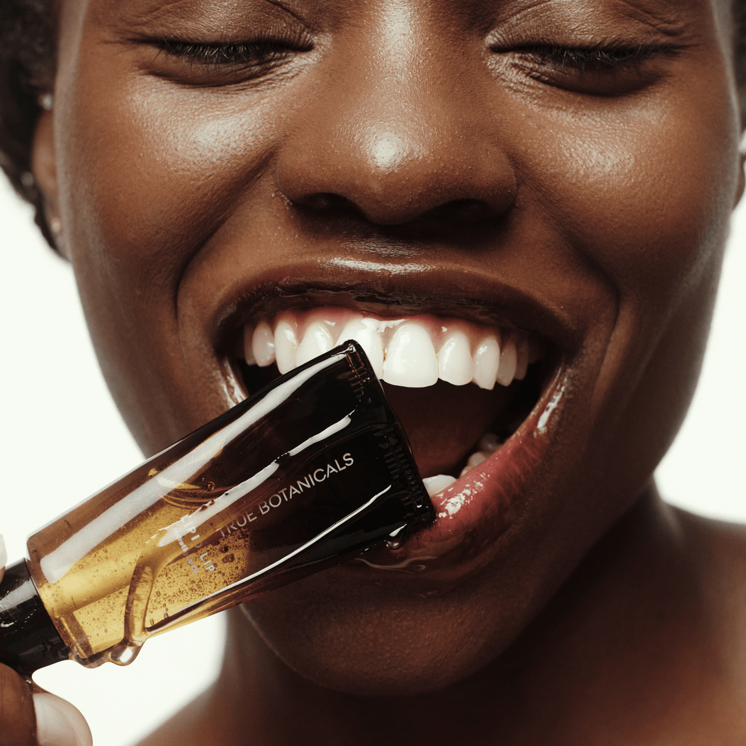 Close-up of a woman with a bottle of True Botanicals lipid lip oil by her mouth.