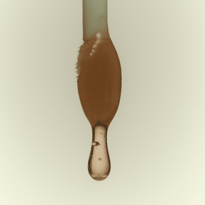 Close-up of a lip oil wand with a droplet of lip oil on a beige background