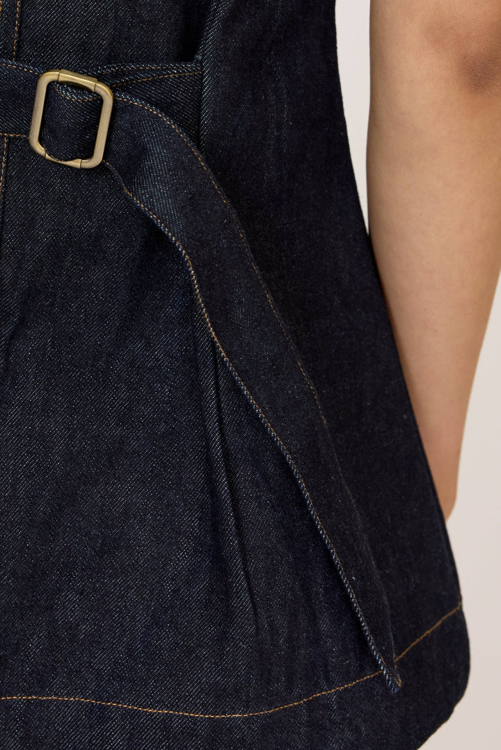 Woman wearing a Laude Longline Vest in Dark Indigo with an adjustable waist buckle over a plain background