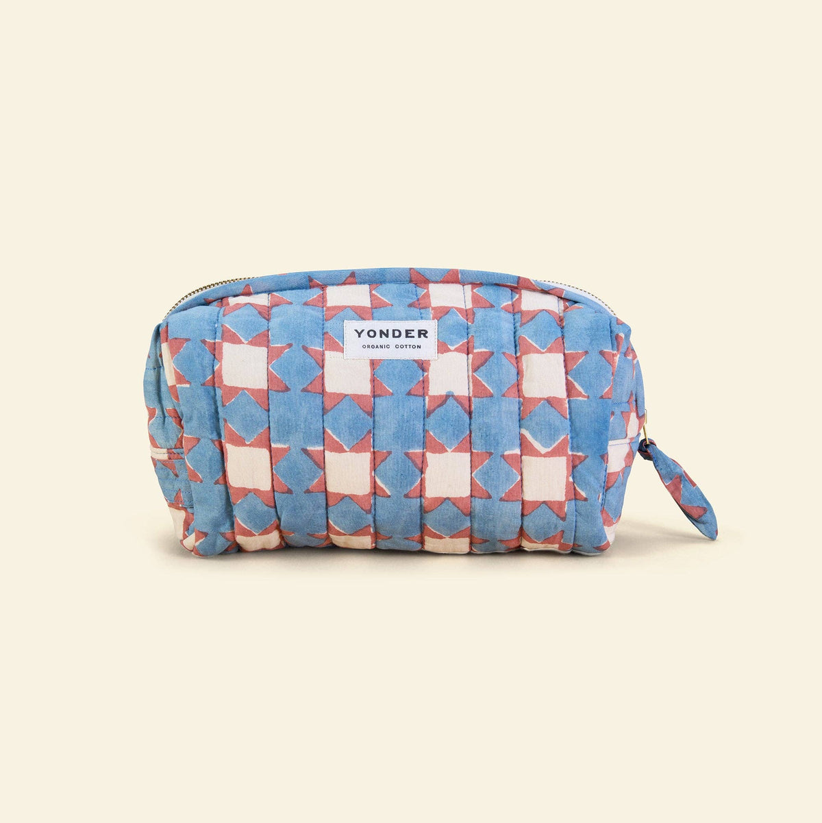 A Yonder wash bag featuring a blue, pink, and white geometric quilted pattern, shown on a solid light beige background.