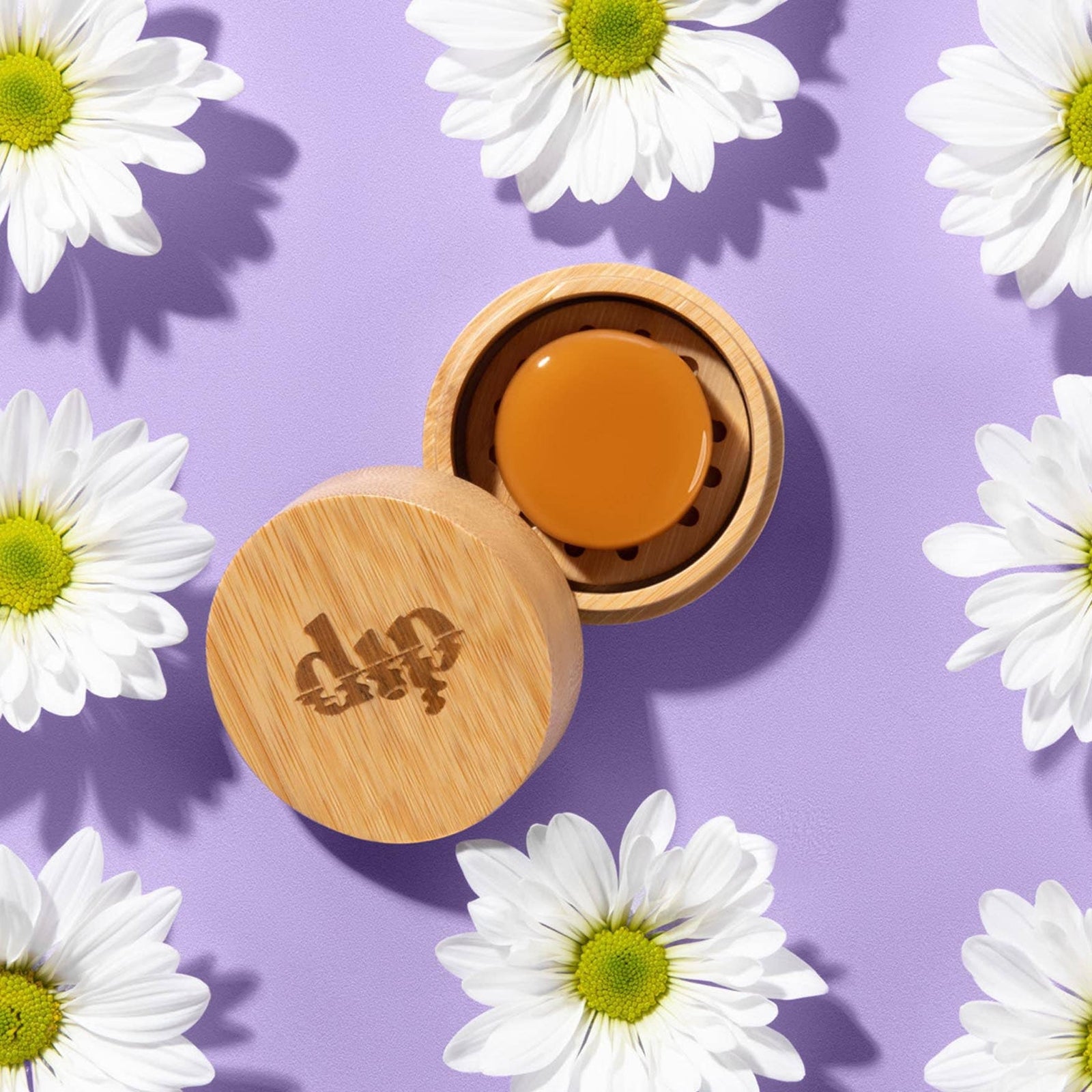 Bamboo container with a lid featuring a Dip logo, filled with a conditioner mini bar surrounded by white flowers on a purple background.