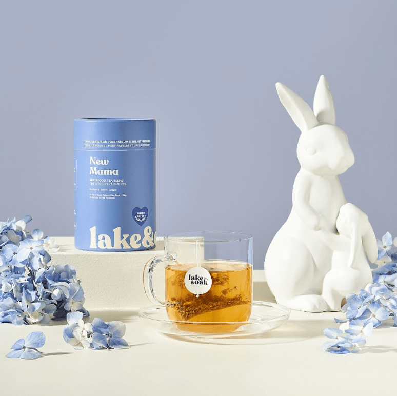 Tea set with 'lake & oak' branding, including a mug, tea canister, and decorative rabbit figure on a light surface with flowers.