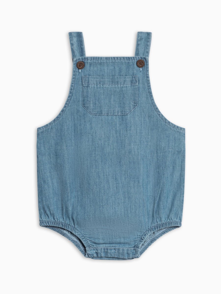 Blue chambray baby romper with straps on a white background