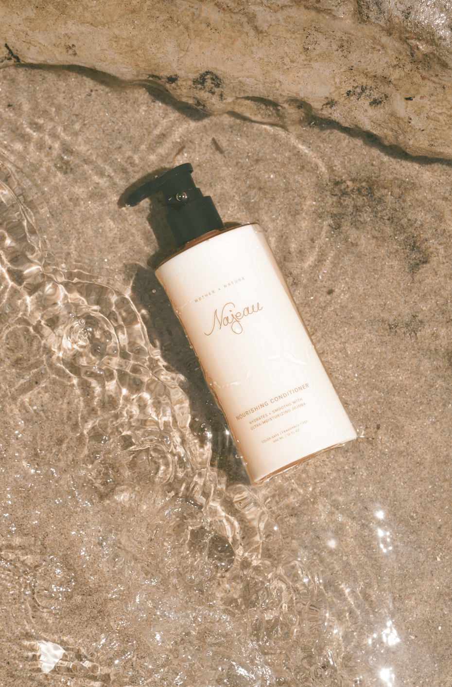 Skincare bottle with Najeau label on a wet stone surface