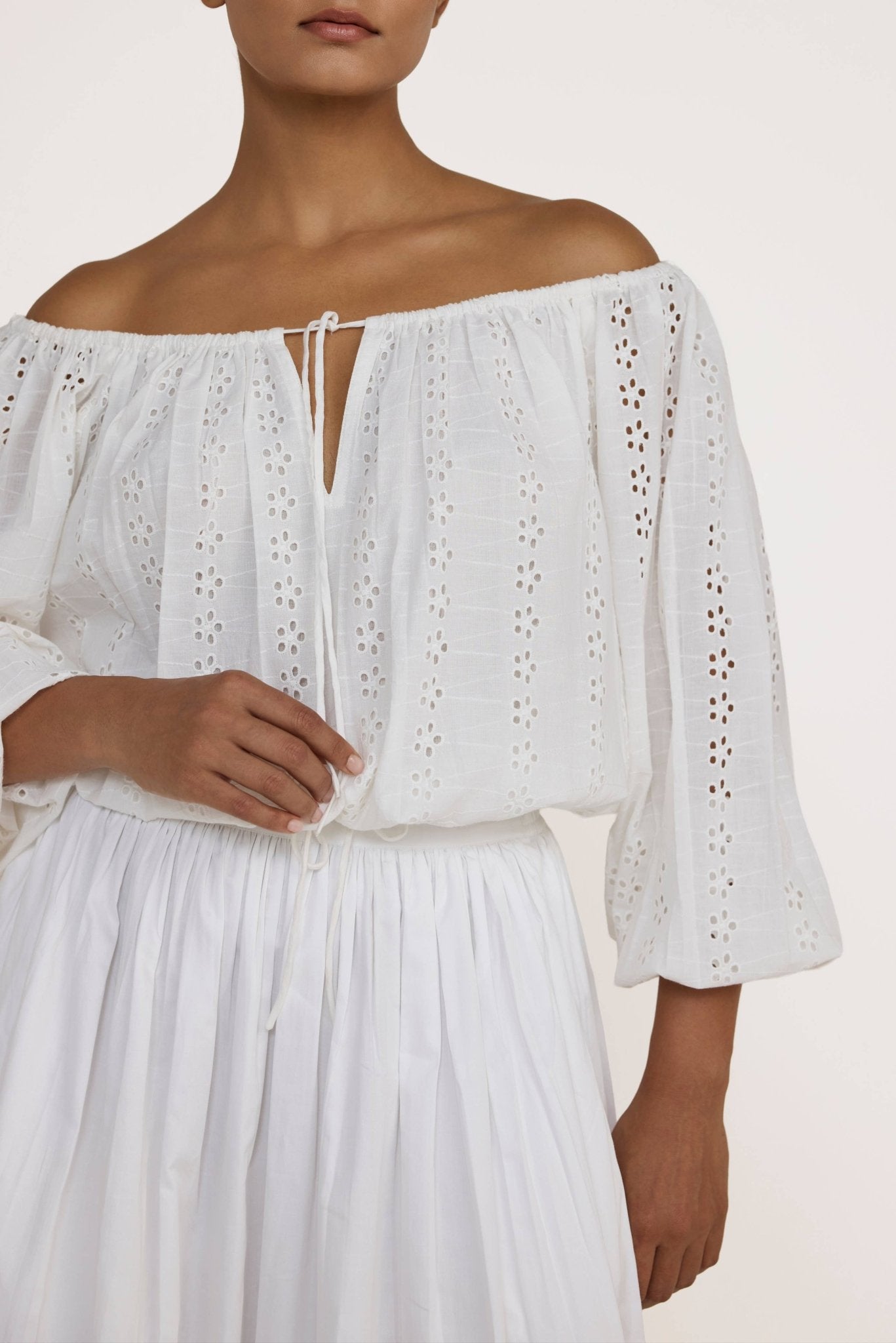 Woman wearing a Laude the Label Off The Shoulder Blouse in Ivory Lace with intricate detailing on a plain background