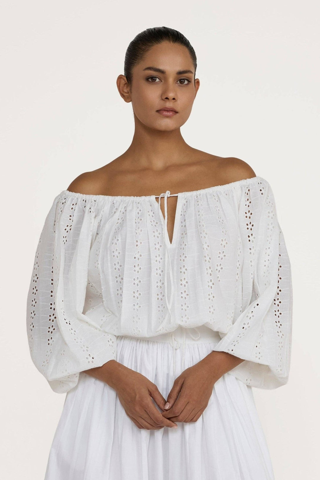 Woman wearing a Laude the Label Off The Shoulder Blouse in Ivory Lace with intricate detailing on a plain background